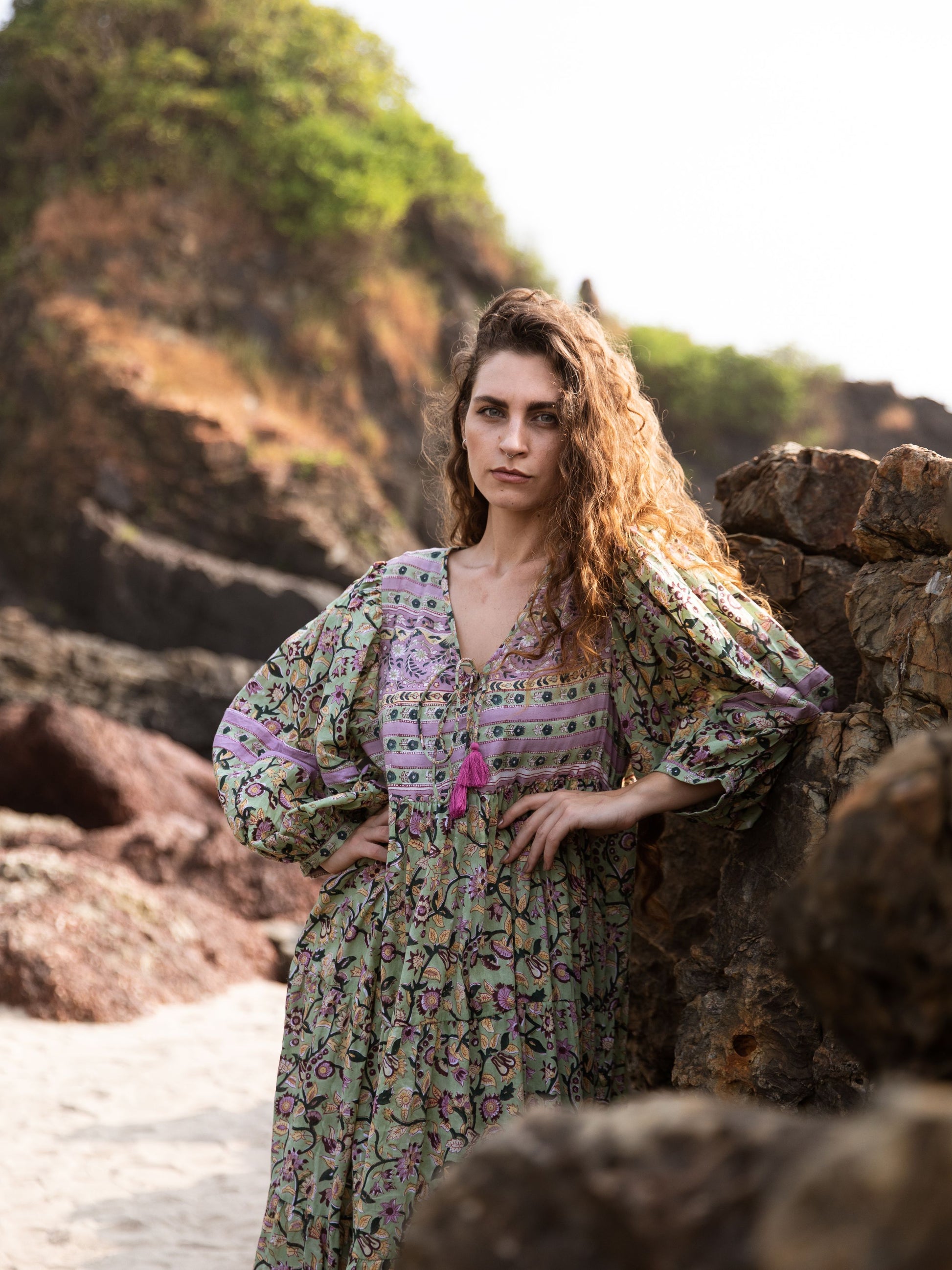 Model showcasing the Ubek Bohemian Dress with seaside rocks in the background.