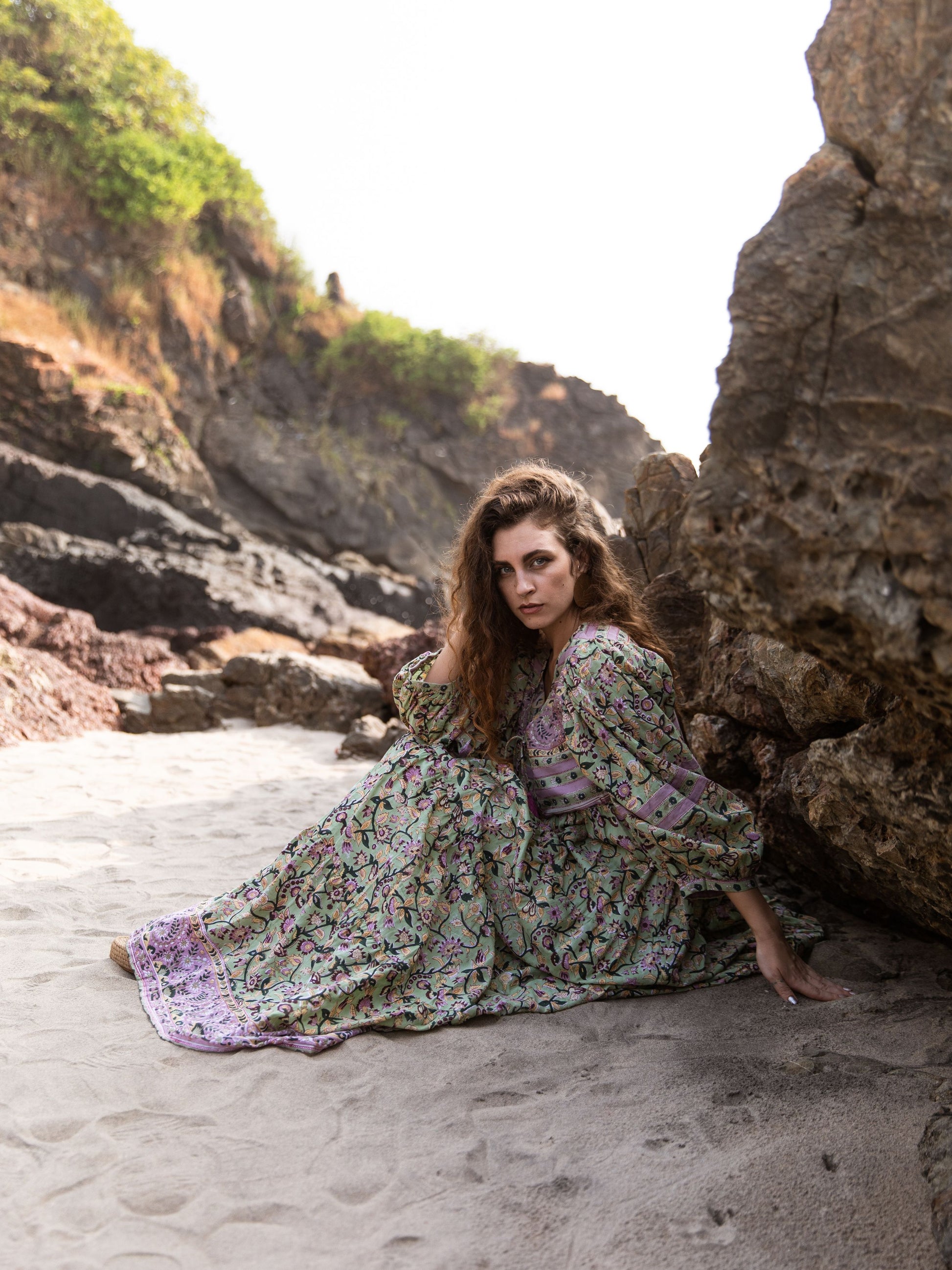 Model seated on beach rocks wearing the Ubek Bohemian Dress.