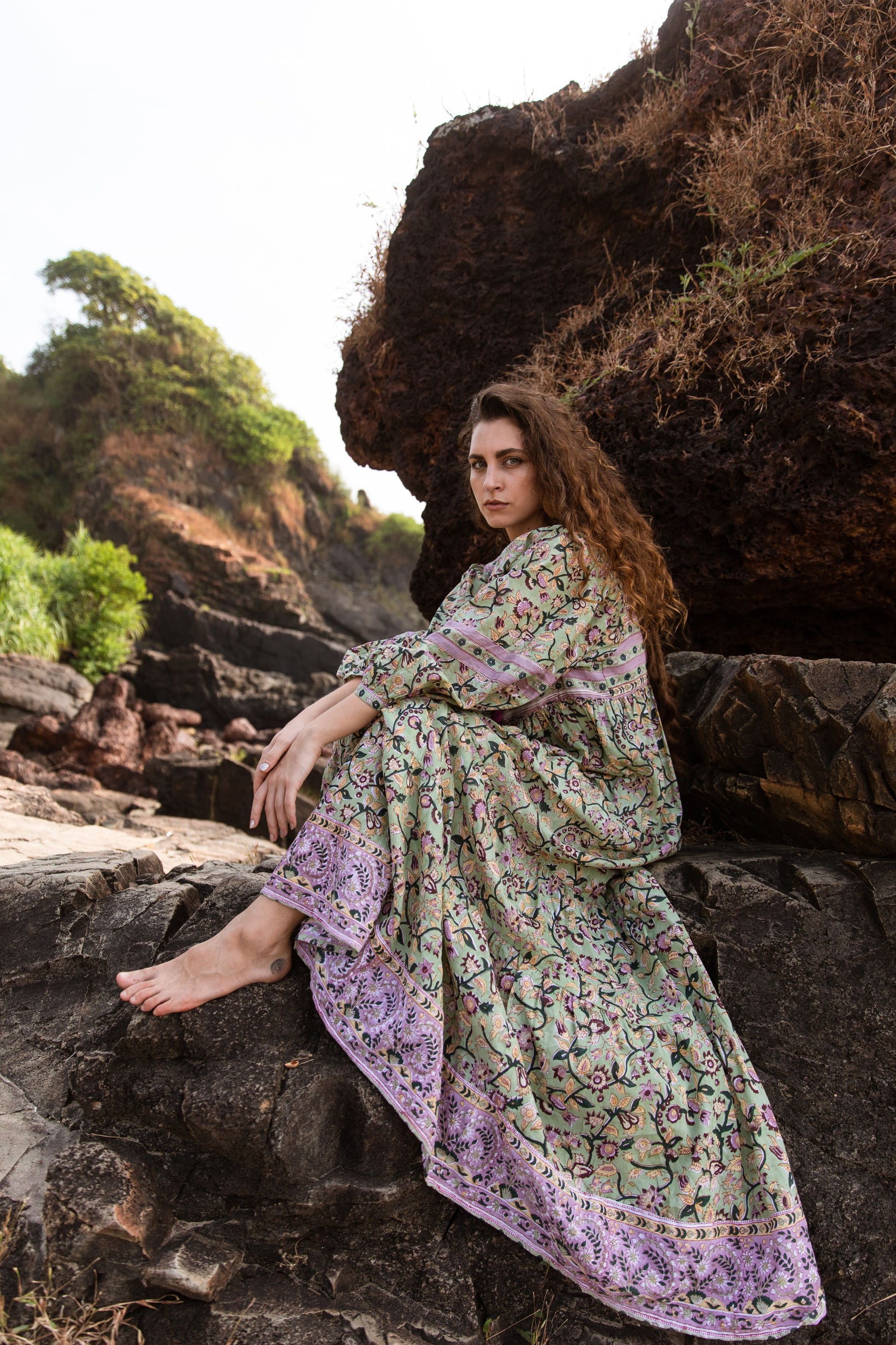 Model seated on beach rocks wearing the Ubek Bohemian Dress.
